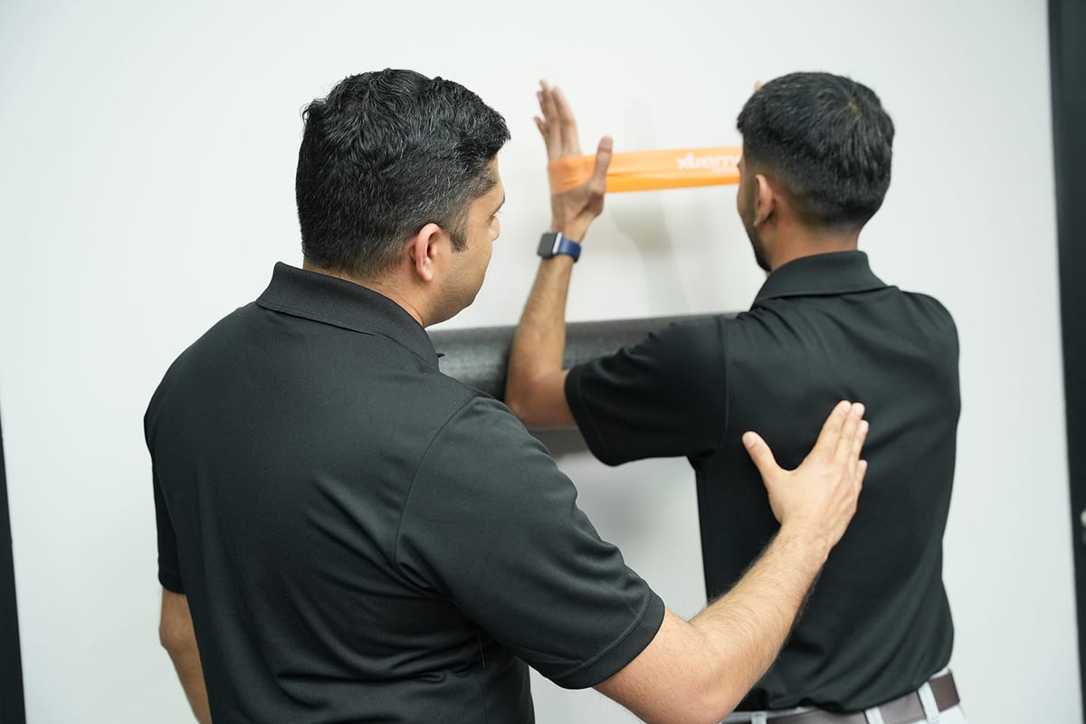 Two Hamilton Physio & Rehab physiotherapists coaching a wall exercise with a resistance band